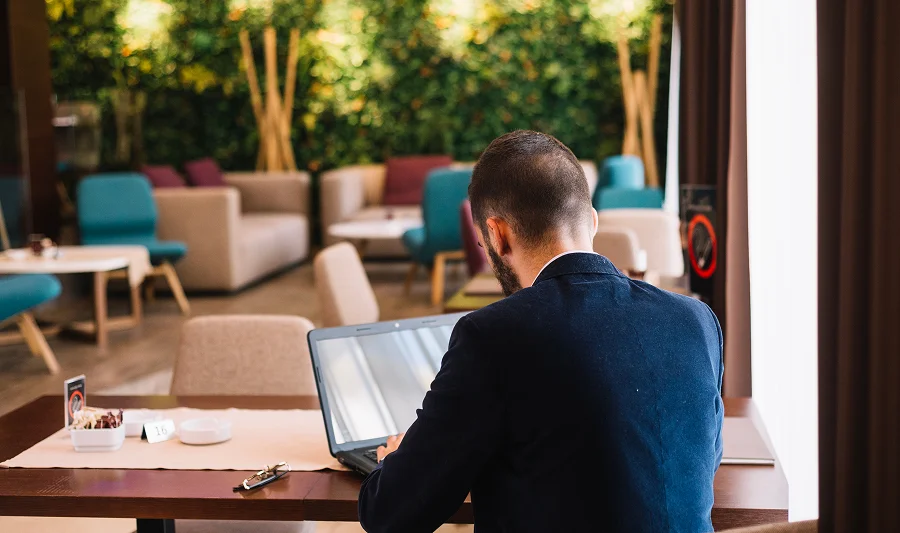 Man in a dark suit working on a laptop, seen from behind, in a modern lounge with a green living wall
