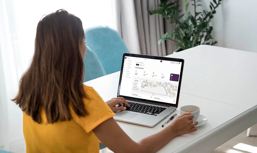 Woman in yellow shirt working on a laptop displaying a property management dashboard at a white table